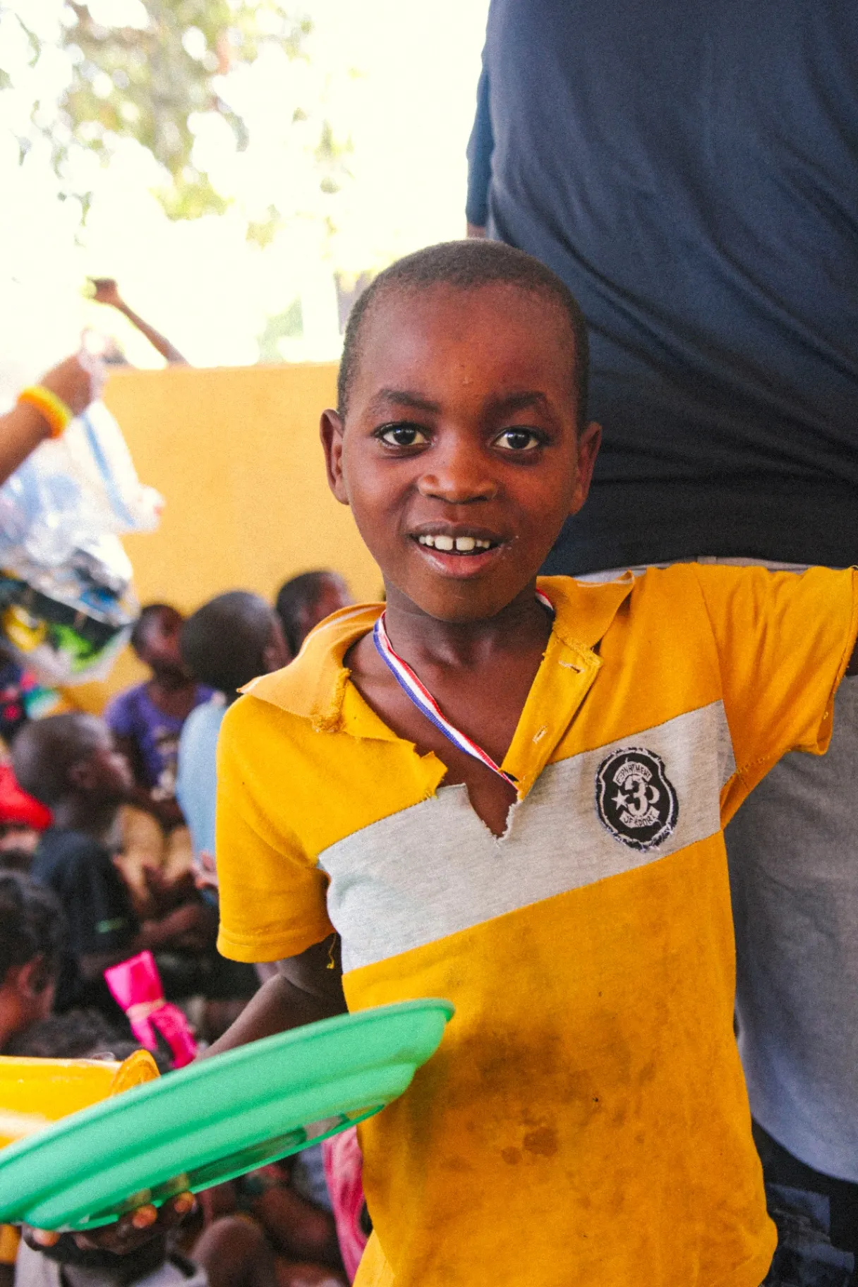 Boy in yellow shirt smiling with a plate